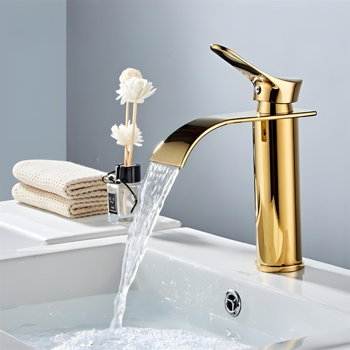 Torneira monocomando dourada de luxo com bica alta estilo cascata em lavatório branco.